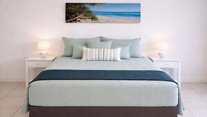 Ein Bett mit Blick auf einen Strand, zwei Nachttische mit Lampen und ein Bild über dem Bett.