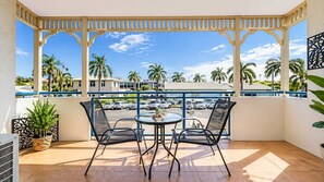 Ein Balkon mit Tisch und Stühlen, Blick auf geparkte Autos und Palmen.