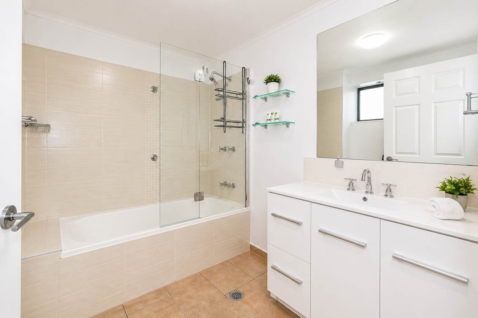 Een moderne badkamer met een douchecabine van glas, een witte wastafel met spiegel en een potplant.