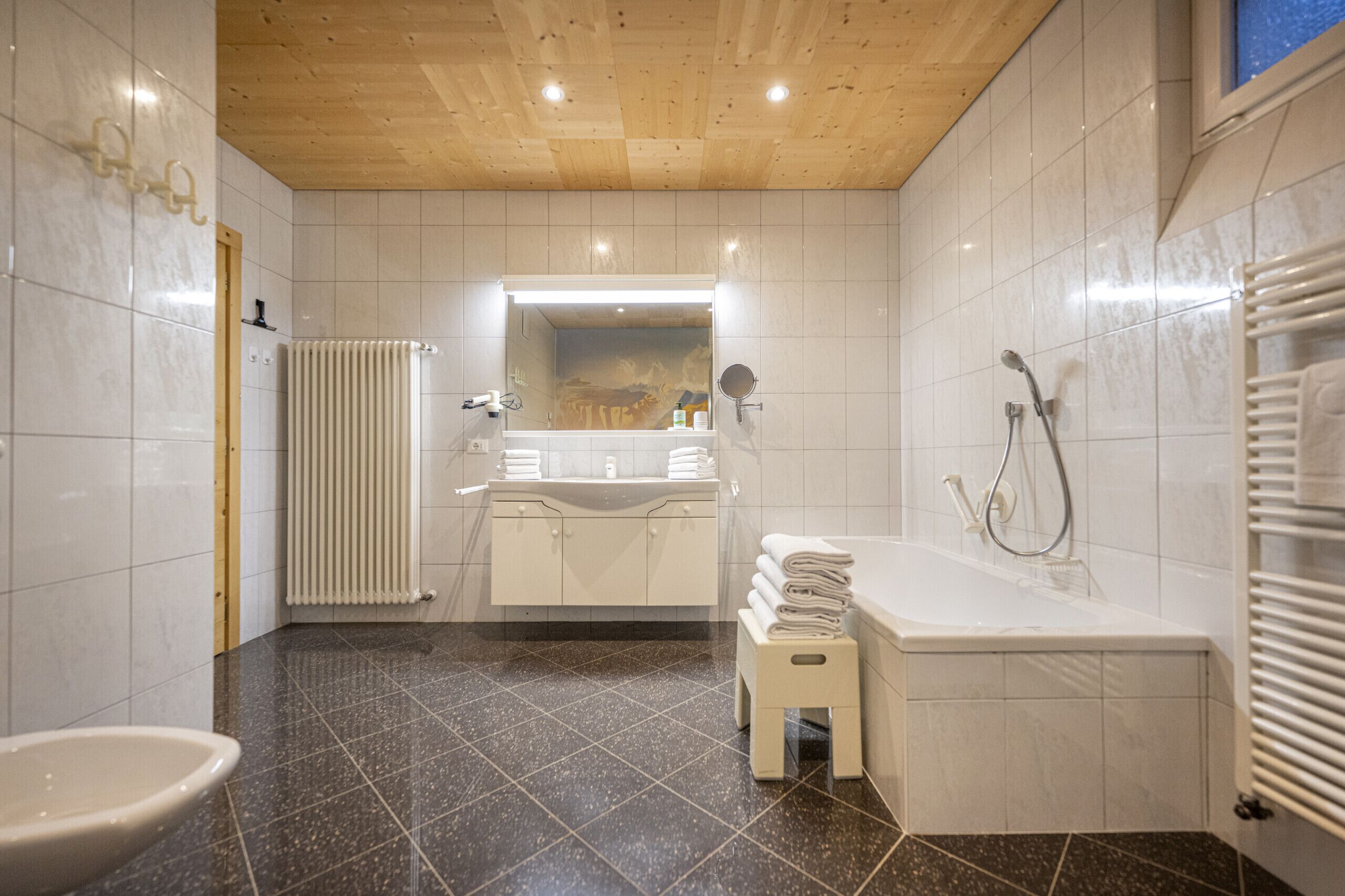 Un baño moderno con techo de madera, azulejos blancos, una bañera, un lavabo y un inodoro.