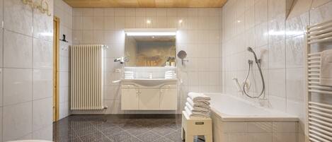 Un baño moderno con techo de madera, azulejos blancos, una bañera, un lavabo y un inodoro.