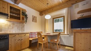 Een houten keuken met een eettafel, stoelen, een bankje en een televisie.