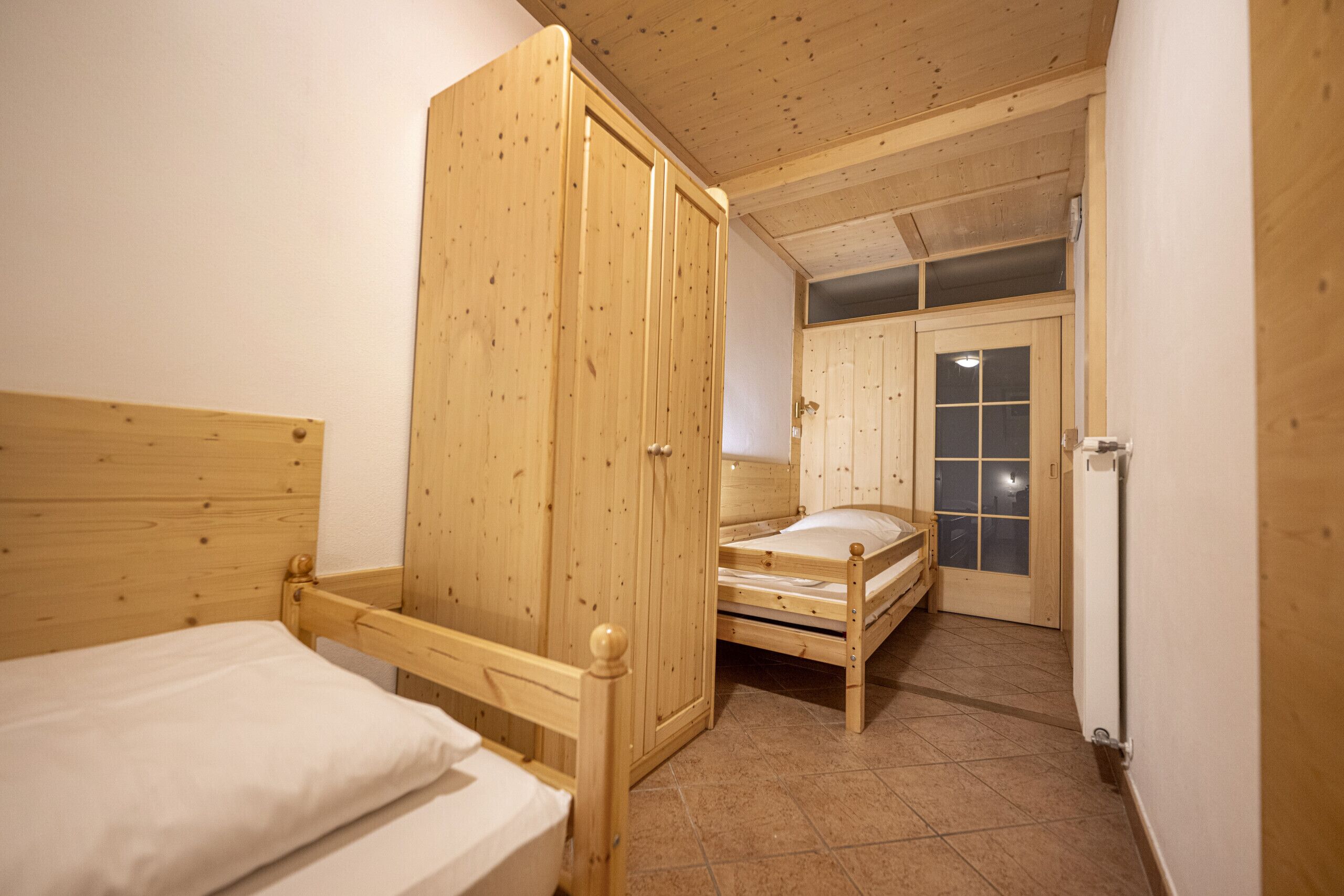 A wooden room with two beds, a wardrobe, and a door leading to another room.