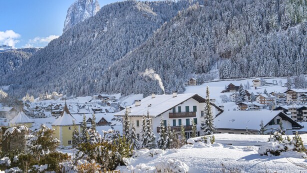 Un village de montagne enneigé, avec des bâtiments traditionnels et un sommet montagneux imposant.