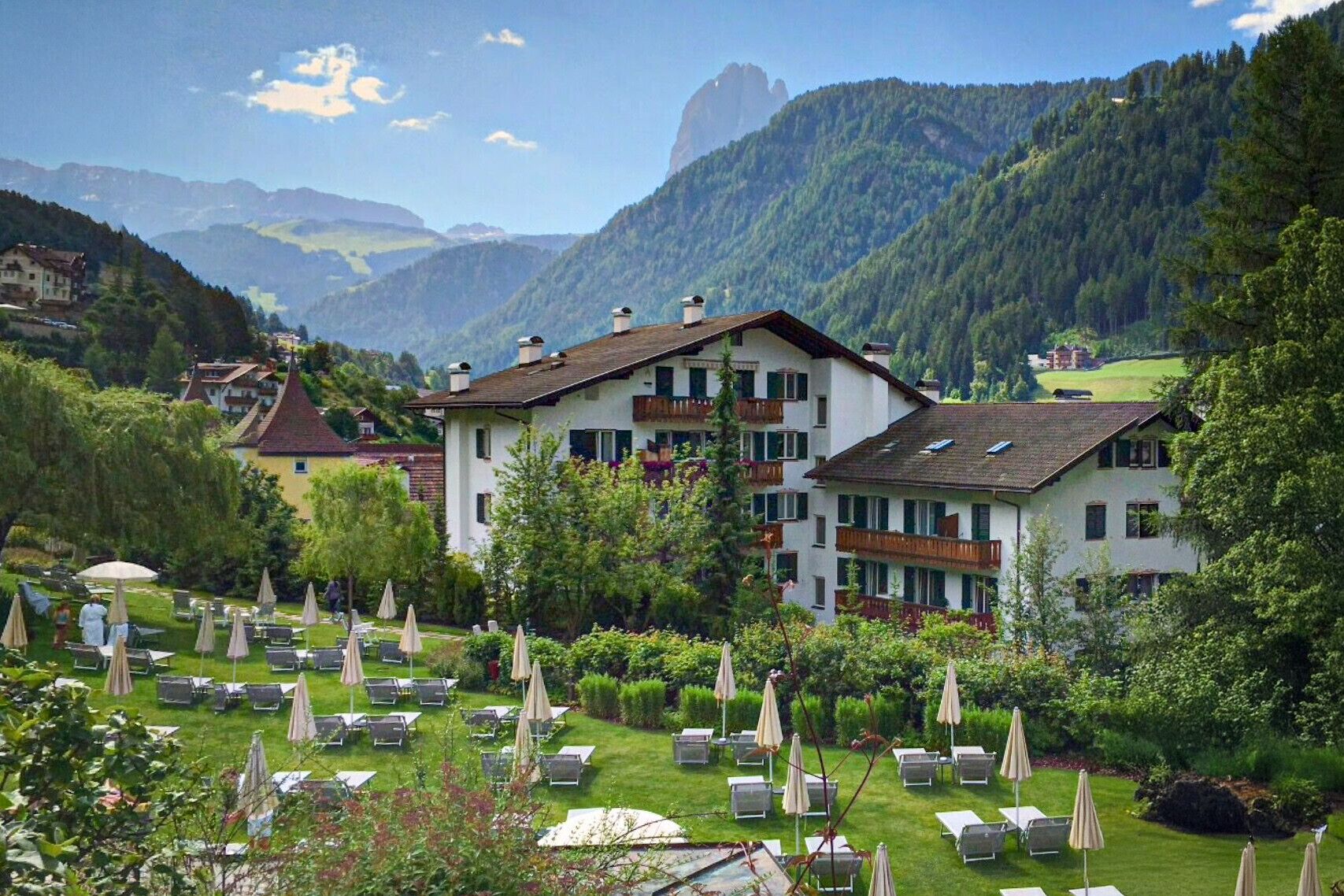 A hotel with a garden area, outdoor seating, and a mountainous backdrop.