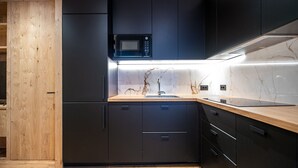 Une cuisine moderne avec des meubles de couleur sombre, une porte en bois, un four à micro-ondes encastré et un dosseret en marbre.