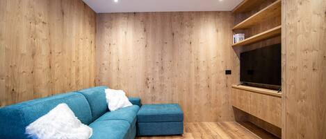 A modern living room with wooden walls, a blue sofa, and a flat-screen TV mounted on the wall.