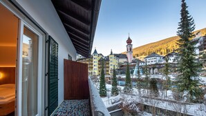 Une chambre d’hôtel avec un balcon donnant sur un village enneigé, une église et une montagne.