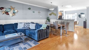 En moderne stue med en blå sofa, et spisebord og et køkken i baggrunden.