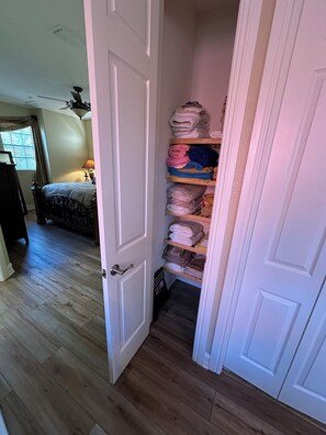Une chambre à coucher avec un lit, une table de chevet, une lampe et une armoire contenant des étagères remplies de serviettes pliées.