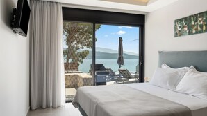 Ein Hotelzimmer mit Bett, Fernseher, Balkon mit Meerblick und einem Bild an der Wand.