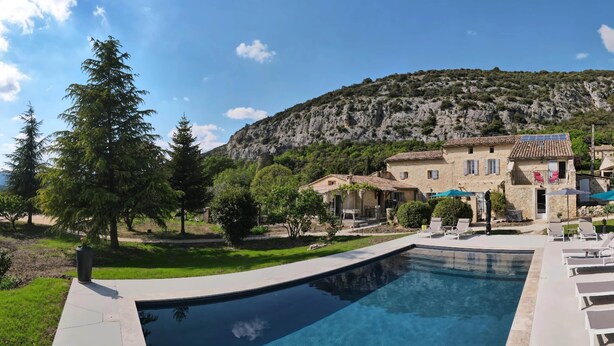 A swimming pool with a patio area, a stone building with a tiled roof, and a mountainous backdrop. - Le Rissas, gite for 4 _ Lacets Ventoux (Beaumont-du-Ventoux)