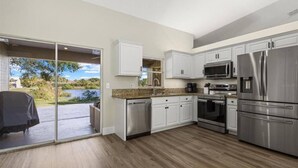 Una cocina moderna con armarios blancos, electrodomésticos de acero inoxidable y vistas a un lago a través de una puerta corrediza de vidrio.