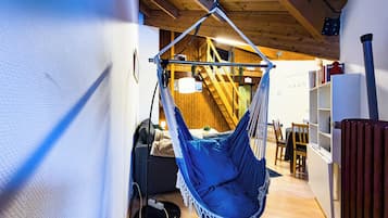 Een kamer met een hangstoel, houten balken, een trap, een boekenkast en een radiator.