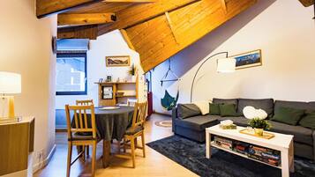 Een gezellige woonkamer met schuine wand, houten meubels, een eethoek en een boekenplank.