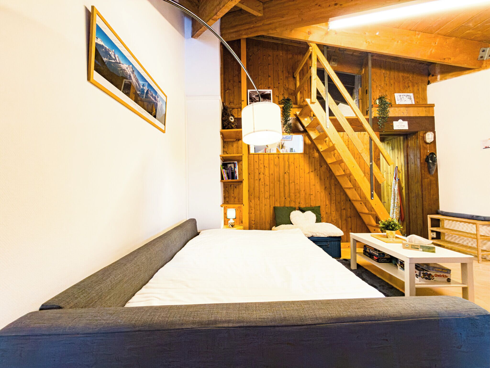 Een knus vertrek met een bed, houten wanden, een trap en een boekenplank.