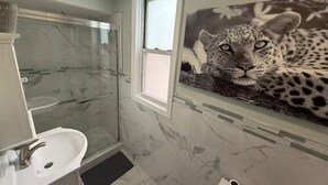 Ein Badezimmer mit Duschkabine aus Glas, einem weißen Waschbecken und einer Wandmalerei mit Leopardenmuster.