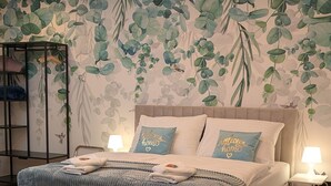 A bedroom with a bed, pillows, a bedside table, and a wall with a leaf pattern. - Green Dream Retreat (Linz)