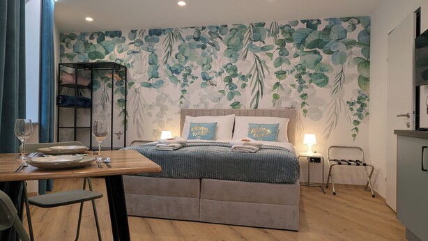 A neatly arranged bedroom with a bed, bedside lamps, a table with plates and a wine glass, and a chair. - Green Dream Retreat (Linz)