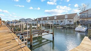 A marina with docked boats, wooden walkways, and residential buildings along the water. - Rustic Harbor I (Ocean City)