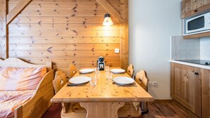 Ein gemütlicher Holzraum mit einem Esstisch für vier Personen, einem Bett mit gestreifter Decke und einer Küchenzeile inklusive Mikrowelle.