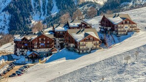 Ein Skigebiet mit mehreren Holzbauten, einem Parkplatz und einer schneebedeckten Piste.