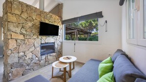 Une cheminée en pierre, un téléviseur à écran plat, une petite table ronde et un canapé avec des coussins verts.