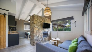 Un espace de vie moderne comprenant une cheminée en pierre, un canapé avec des coussins, un coin repas et une cuisine.