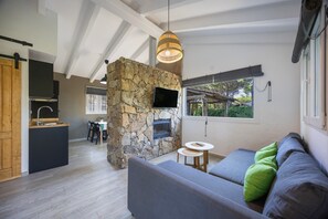 Ein stilvoller Wohnraum mit Kamin aus Stein, einer Couch mit Kissen, einem Essbereich und einer Küche.