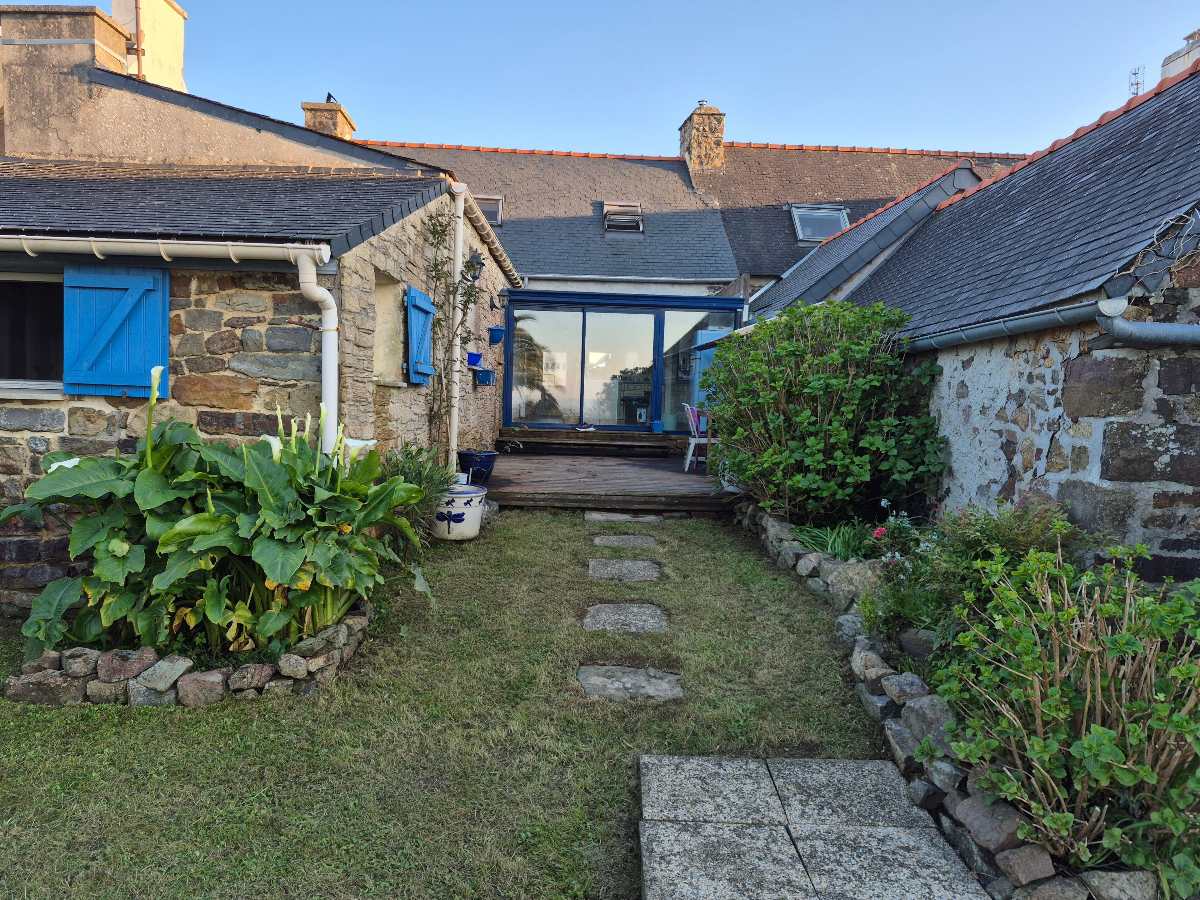 A stone house with a wooden deck, a glass door entrance, and a small garden with stepping stones.