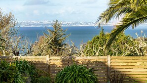 Vista sulla costa con una recinzione di legno, vegetazione e un paesaggio urbano in lontananza.