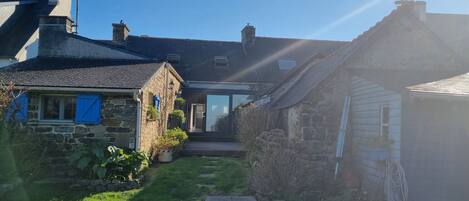 A stone house with a wooden door, a small garden, and a clear blue sky.