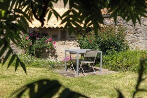 A garden with a table and chair, a stone wall, and flowering plants. - Quiet house with garden - ideal for a relaxing stay (Persac)