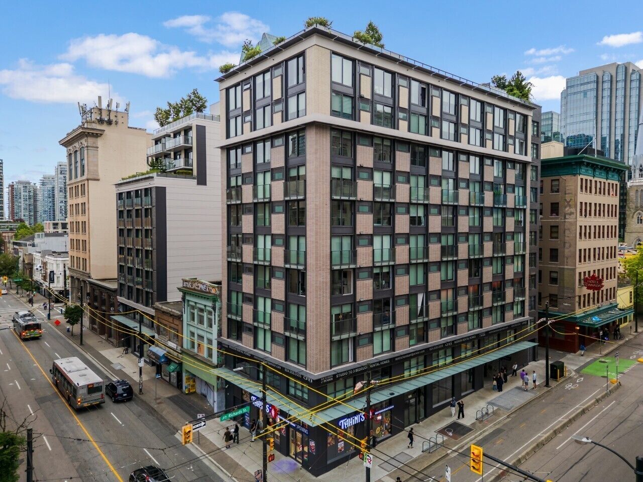 Un immeuble à plusieurs étages, doté d’un style architectural moderne, avec une façade combinant verre et brique, situé dans un environnement urbain, le long d’une rue.