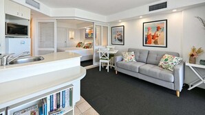 A compact living space with a kitchenette, a grey sofa, a dining table, and a bookshelf. - It's Five O'Clock Somewhere (Sunshine Coast)