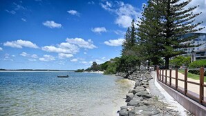 A coastal walkway with a rocky edge, clear water, and a distant view of a building. - It's Five O'Clock Somewhere (Sunshine Coast)