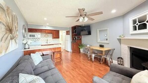 A modern living room with a gray sofa, a fireplace, and a dining area with a table and chairs. - River Front Condo Walking Distance to Downtown (New Braunfels)