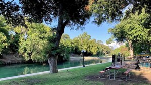 A park with a picnic table and benches, a walking path, and a body of water. - River Front Condo Walking Distance to Downtown (New Braunfels)