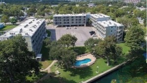 A multi-story building with a parking lot and a swimming pool surrounded by trees. - River Front Condo Walking Distance to Downtown (New Braunfels)