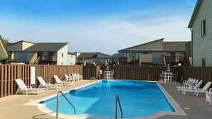 Una piscina rettangolare con un solarium in legno e poltrone relax.