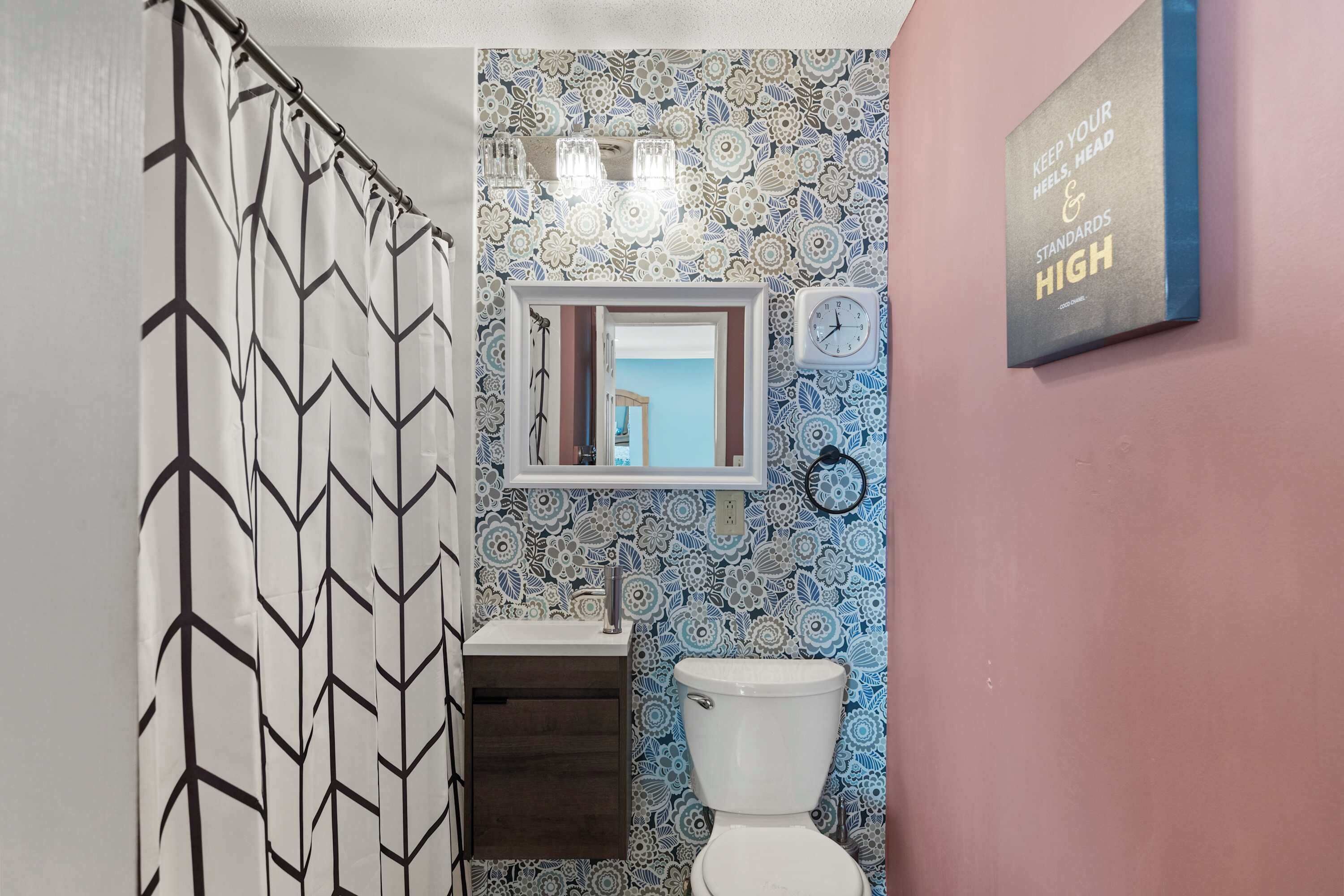 Un baño con cortina de ducha, lavabo, inodoro, espejo y un reloj de pared.