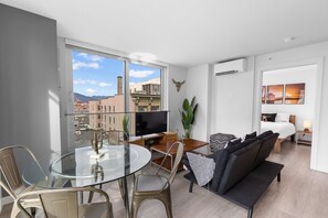 Ein modernes Wohnzimmer mit einem Glastisch, einer Couch, einem Fernseher und einem Balkon mit Blick auf die Stadt.