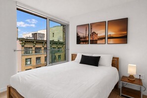 Une chambre d’hôtel avec un grand lit, une table de chevet avec une lampe et une vue sur les bâtiments par une grande fenêtre.