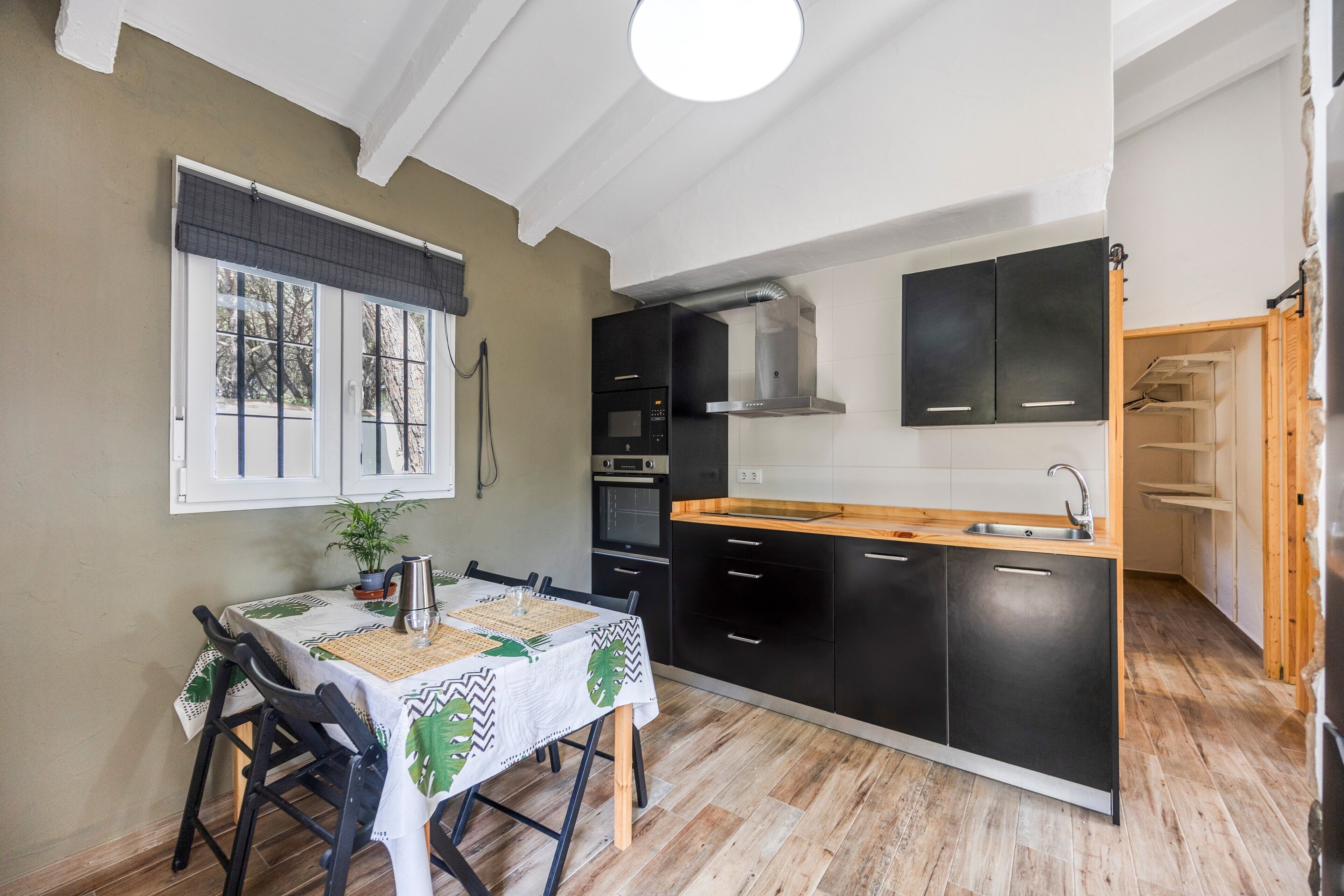 A compact kitchen with black cabinets, a wooden countertop, and a dining area with a table set for two.
