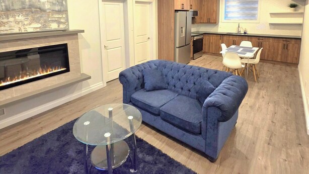 A modern living room with a fireplace, a blue sofa, and a glass coffee table. - Staycation Presidential Apartment- Free Parking (London)