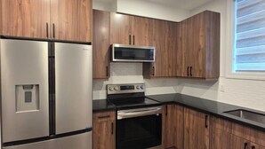 A modern kitchen with wooden cabinets, stainless steel appliances, and a black countertop. - Staycation Presidential Apartment- Free Parking (London)