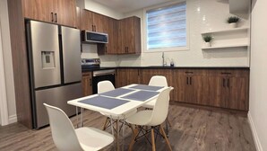 A modern kitchen with wooden cabinets, stainless steel appliances, and a dining area with white chairs and a table. - Staycation Presidential Apartment- Free Parking (London)