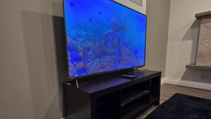 Un televisor de pantalla plana sobre un soporte negro en una habitación con piso de madera y alfombra negra.