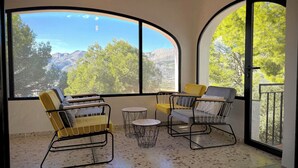 A room with large arched windows, two chairs, a small round table, and a view of mountains and trees. - Villa Horizonte with pool and pool house, mountain and nature views (orba)