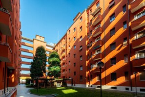 Un immeuble résidentiel à plusieurs étages, doté de balcons, d’une cour intérieure arborée et surplombant un ciel dégagé.